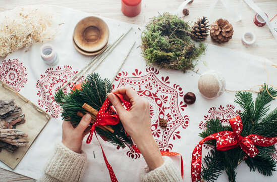 Christmas Season - Overhead Shot of Woman Tying Cinnamon Sticks and Fir Twigs to Big Red Candle