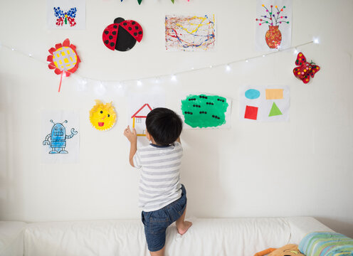 Little boy hang up his artwork on the wall