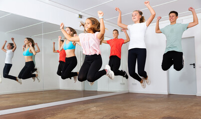 Cheerful teenage boys and girls jumping together while dancing synchronous group choreography in...