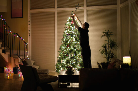 Man reaching up to put the star on the Christmas tree at night