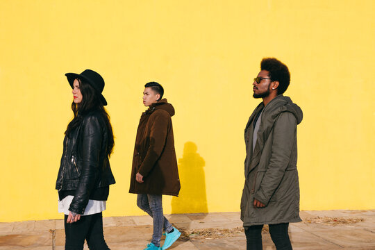 Side view of friends walking in front of a yellow wall on winter.
