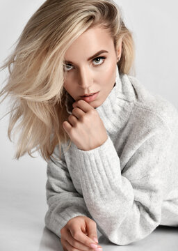 Portrait of young sexy flirting blonde woman vamp in warm knitted sweater looking at camera touching her lips