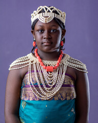 African girl dressed in Ewu-Ivie the beaded top, Ivie-uru and damask, traditional attire of benin on colored background - obrazy, fototapety, plakaty