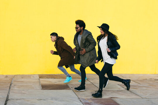 Side view of group of friends running in front of a yellow wall.