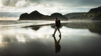 Walking on Bethells beach with reflection on the wet black sand, Waitakere, Auckland