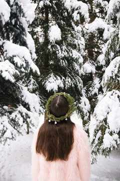 Back view of young woman in Christmas wreath looking up on snowy fir trees