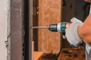 The carpenter drills holes in the wall and the metal door frame with a drill, later screws the...