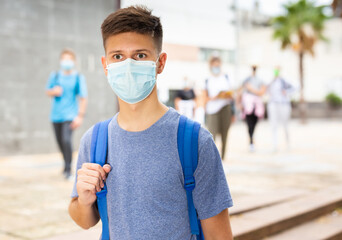 Fototapeta na wymiar Portrait of teenager in protective mask with backpack going to school lessons on sunny autumn day. New lifestyle during coronavirus pandemic