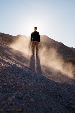 young man standing tall with sunlight at his back and dust flying around him