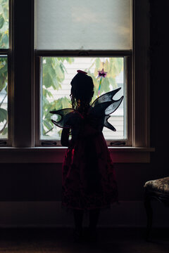 African American girl with fairy wings looking out the window