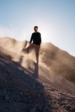 young man standing tall with sunlight at his back and dust flying around him