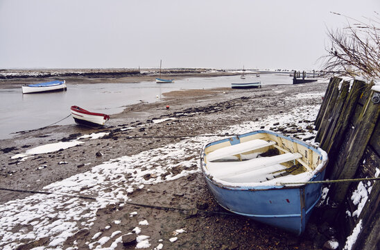 Boats and snow at low tide. Burnham Overy Staithe, Norfolk, UK.