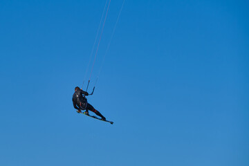 Kitesurfer in wetsuit in  the jump on a background of blue sky