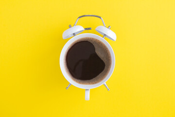 Black coffee on the dial of the white alarm clock in the center of the yellow background