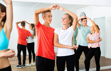 Group of happy cheerful smiling teenage boys and girls training movements of slow foxtrot in dance...