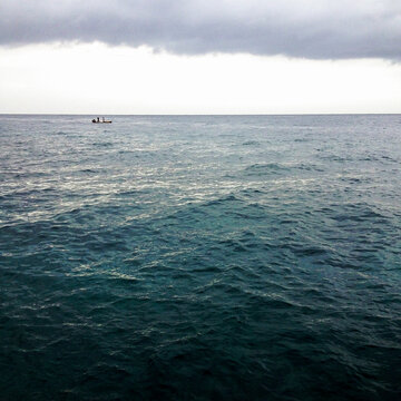 A tiny fishing boat in the vast Caribbean Sea beneath a layer of clouds.