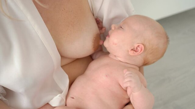 close up. mother feeds baby sitting at home in white interior. breast-feeding.