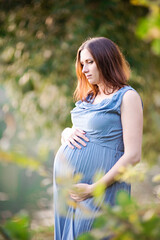 Fototapeta premium Beautiful pregnant woman outdoors, with pleasure expecting baby and having happy pregnancy time