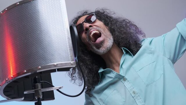 African vocal artist wearing a blue shirt emotionally writing song in the recording studio. Isolated on a blue background.