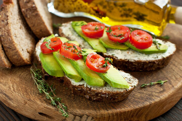 Healthy toast with cream cheese, avocado, cherry tomatoes on rustic wooden table. Selective focus, close up