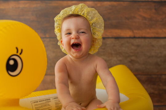 One year old baby girl takes a bath. With yellow duck. First birthday decoration for photoshoot. Shower cap on her head. 
