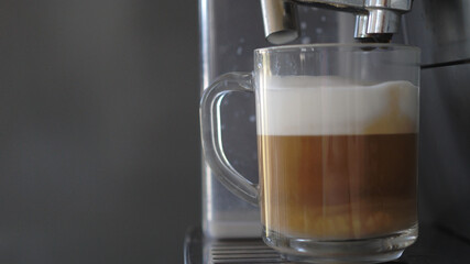 Process of making coffee by coffee machine into glass transparent cup, latte coffee coming out from...
