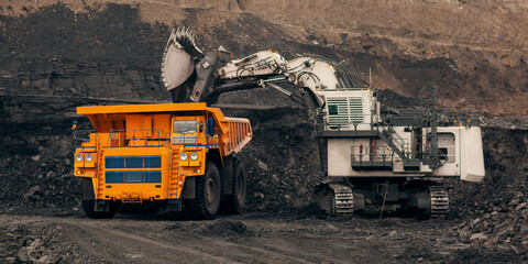 A huge excavator loads rock formation into the back of a heavy mining dump truck. Open pit coal...