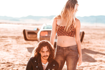 A young couple stands in the middle of the desert looking less than hopeful