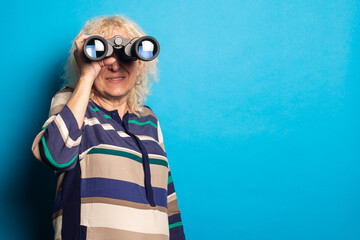 Smiling old woman in a striped dress looks through binoculars on a blue background