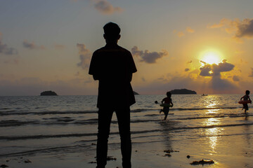 Lonely man stands on the beach looks towards the sun light