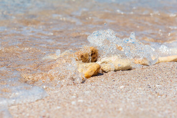 Yellow stones on the sand close-up, covered by the sea wave, splashes.