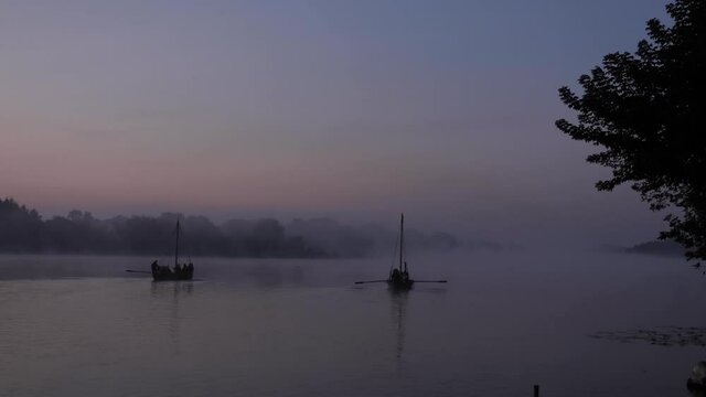 Two ancient authentic wooden boats on a lake or river in the morning during a foggy dawn. Footage shot with natural morning lighting in 4K background with constant focus