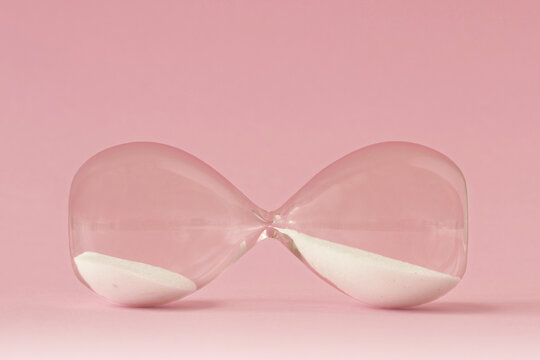 Hourglass lying on pink background - Concept of time and woman