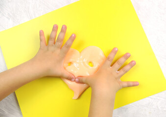  child's hands made funny heart from  slime , hammer slime,  yellow background         