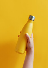 Close up of female hand, holding yellow reusable steel bottle on yellow background