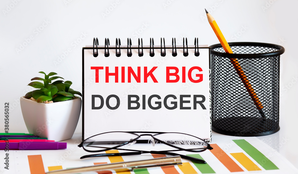 Poster think big do bigger word with notepad on white background with markers ,charts and glasses