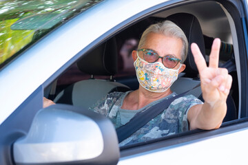 Naklejka premium Attractive senior woman with white hair wearing surgical mask gesturing ok with hand while driving her car
