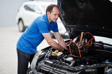 Fototapeta na wymiar Car repair and maintenance theme. Mechanic in uniform working in auto service, checking engine.