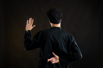 Young male dressed in a black chef suit showing cross finger from behind