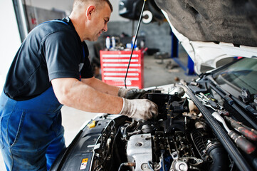 Car repair and maintenance theme. Mechanic in uniform working in auto service, checking engine.