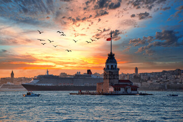 Fototapeta premium Fiery sunset over Bosphorus with famous Maiden's Tower (Kiz Kulesi) also known as Leander's Tower, symbol of Istanbul, Turkey. Scenic travel background and cruise ship for wallpaper or guide book.