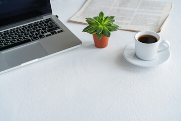 there is a laptop on the table, a mug of coffee and a newspaper