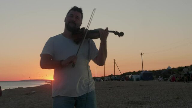Violinist plays the violin on the beach during wonderful sunrise. Low angle view.