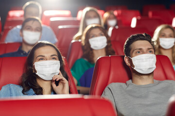 cinema, entertainment and pandemic concept - people wearing face protective medical masks for...
