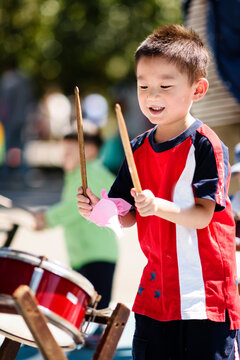 Child holding drumstick and playing drum in sunlight