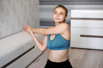 Fototapeta na wymiar Fitness, home and diet concept. Smiling girl streching on floor at home. Stretching the arms and shoulders