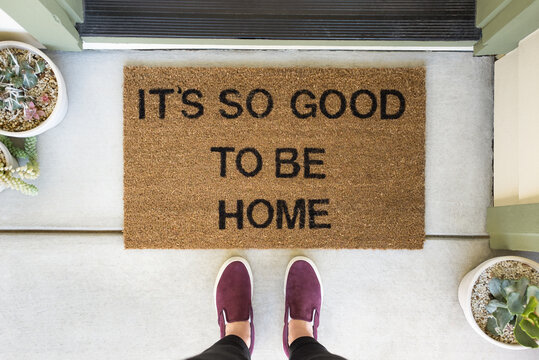 Woman standing in front of a doormat reading ___It___s so good to be home__ÔøΩ