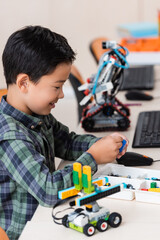 Selective focus of asian schoolboy holding building block near robots in classroom