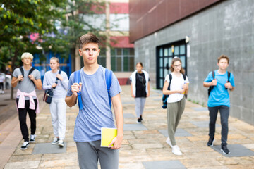 Confident teen boy with backpack walking to college campus in autumn day. Back to school concept.