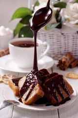 Chocolate icing pouring on freshly baked homemade cake lying on a white saucer